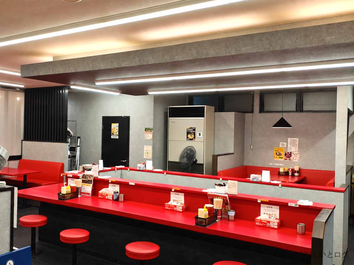 群馬県伊勢崎市にある王道家直伝 との丸家 伊勢崎店の赤いカウンター席とテーブル席が並ぶ店内