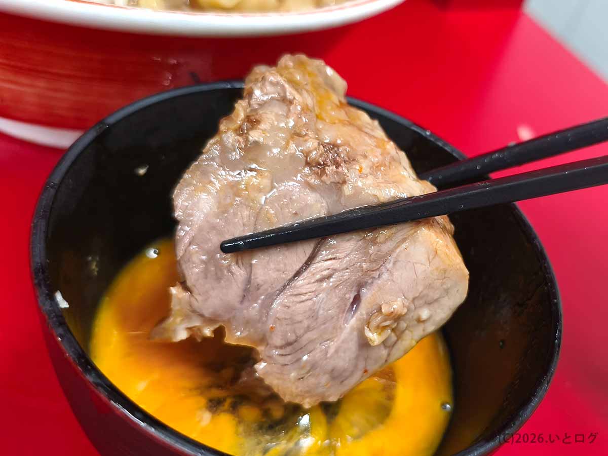ラーメン二郎 大宮公園駅前店の厚切り豚を生卵につけて食べる様子