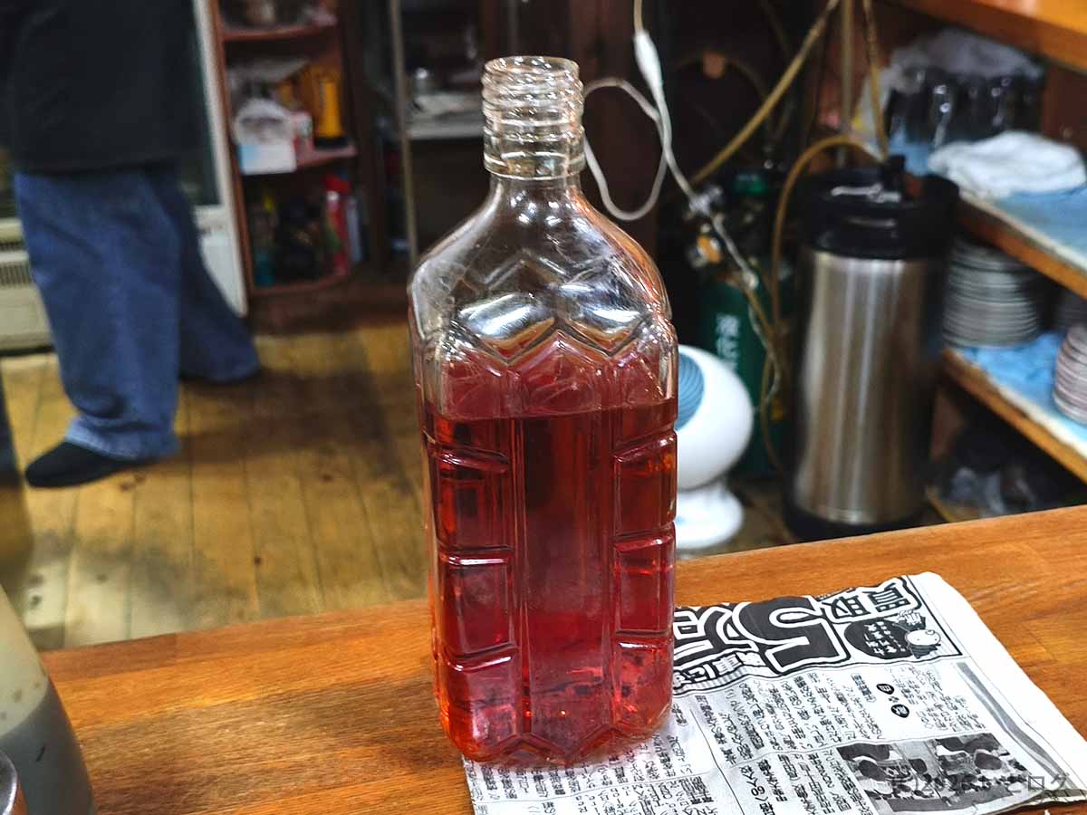 甲府の老舗居酒屋どてやき下條で提供される、赤い梅割りのボトル