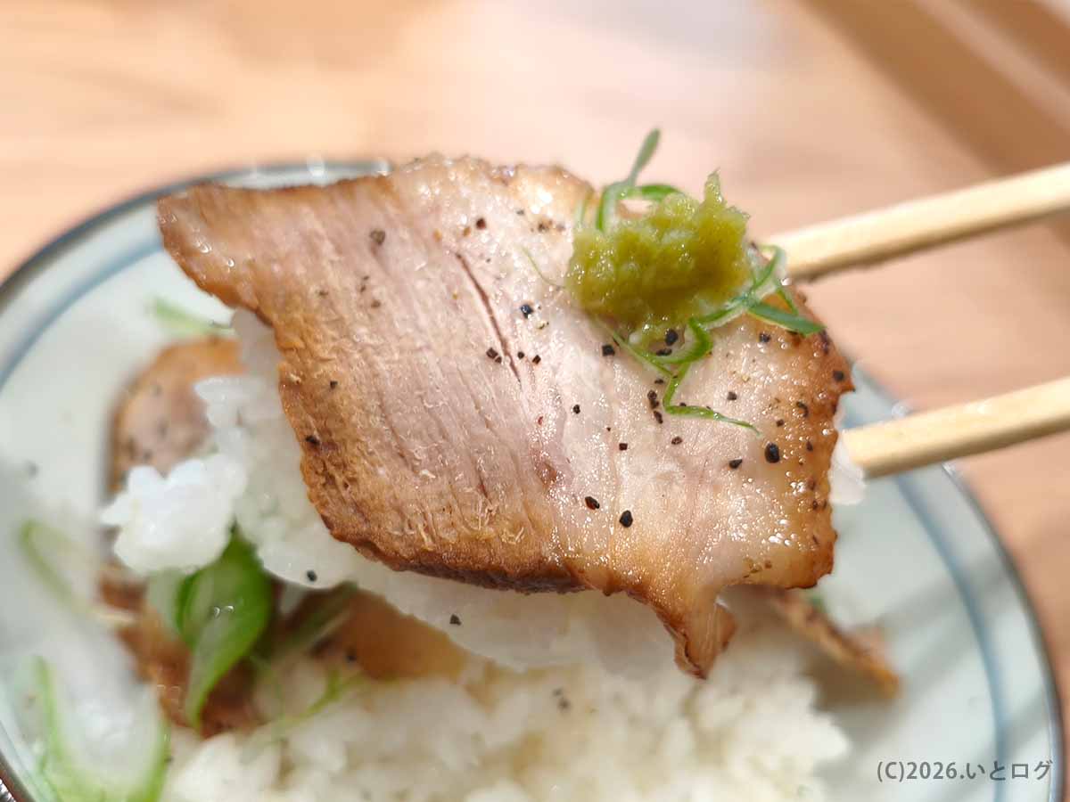 初志貫徹 甲斐竜王店の炙りチャーシューご飯に盛られた、香ばしく焼かれたチャーシューをわさびとねぎとともに持ち上げた様子