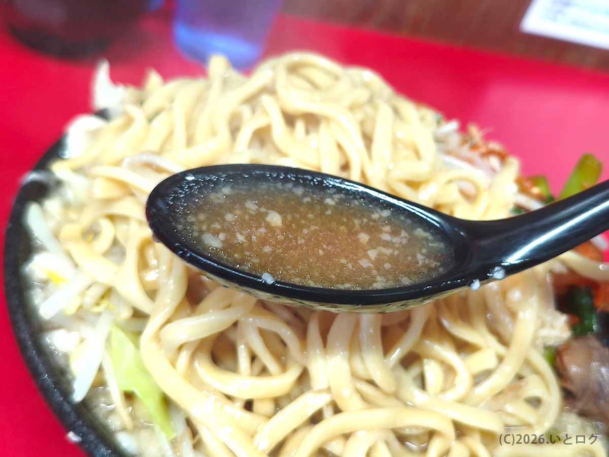 ラーメン二郎 新潟店のスープを黒いレンゲですくった写真。茶褐色のスープに細かな脂が浮かんでいる。