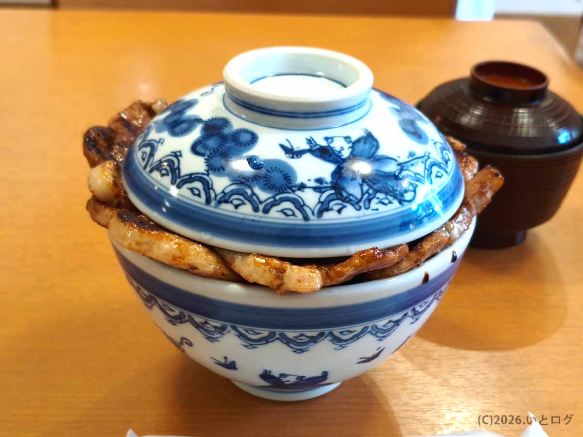 帯広の人気店・元祖豚丼のぱんちょうで提供された豚丼。青い模様の丼の蓋から香ばしく焼かれた豚肉がはみ出している。