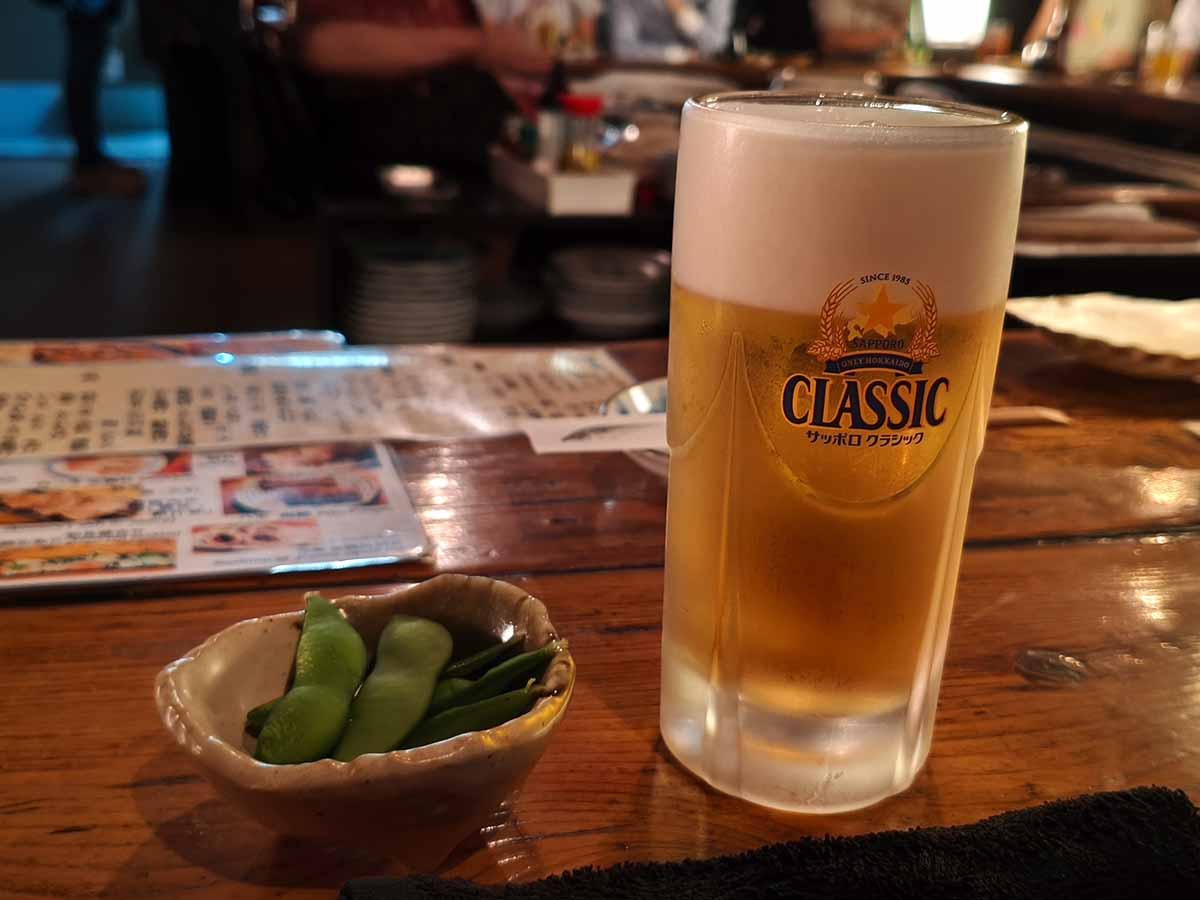 炉ばたの木製カウンターに置かれたサッポロクラシックの生ビールと、小鉢に盛られた枝豆
