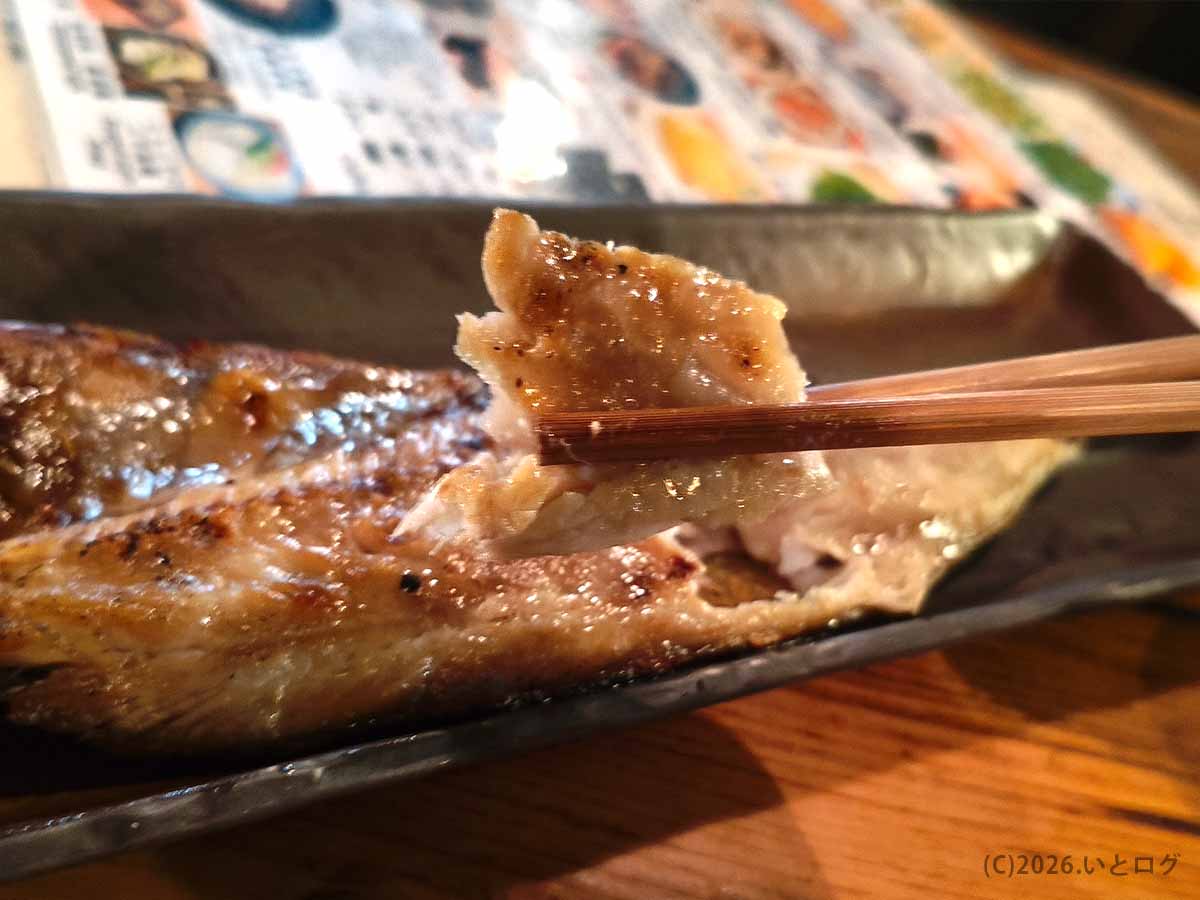 炉ばたで提供された焼き魚を箸で持ち上げた様子。焼き色のついた皮と、ほぐれた白身が写っている