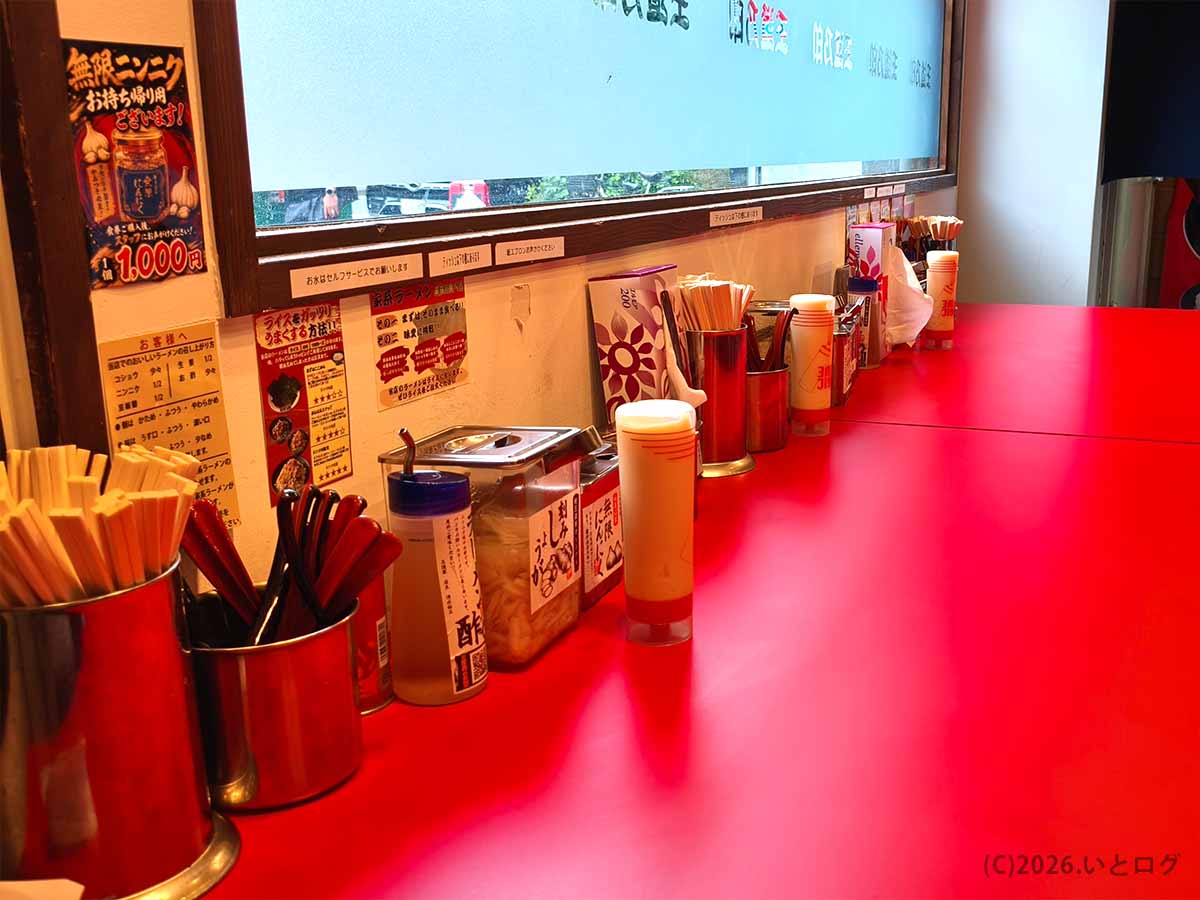 天満の家系ラーメン店「王道乃印 天神家」の赤いカウンターと卓上に並ぶ調味料