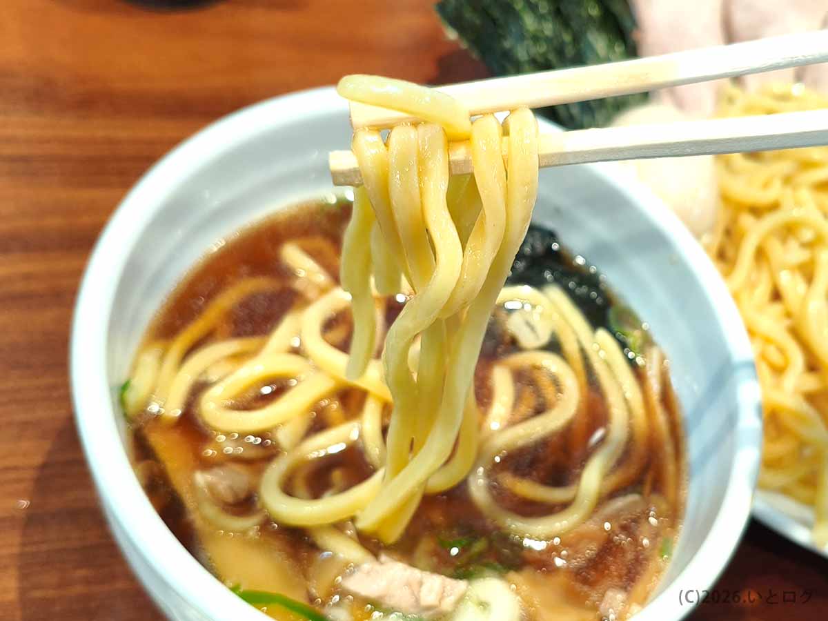 つけそば七福の太めの麺を醤油ベースのつけ汁につけて味わう様子