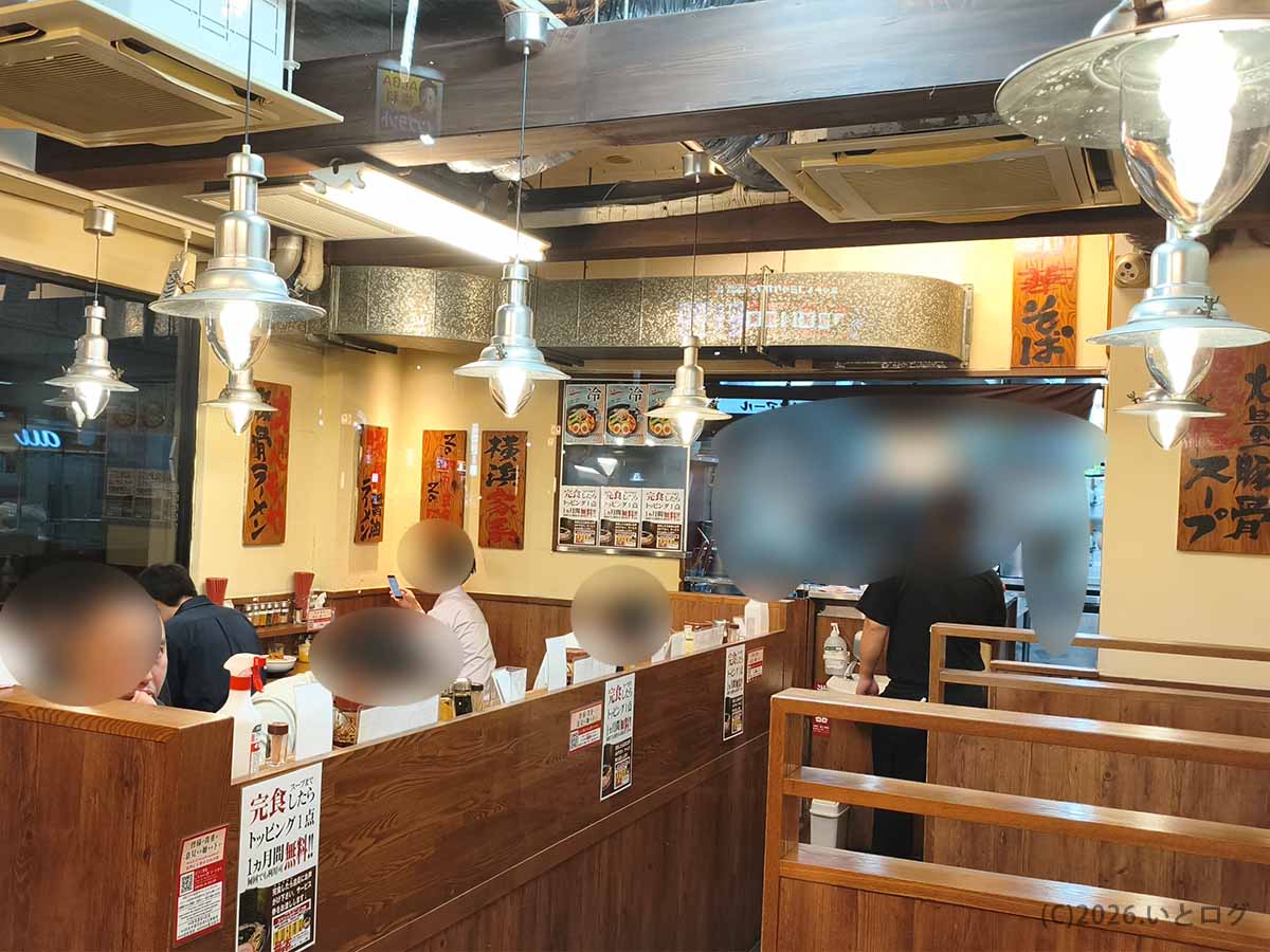 東京都豊島区巣鴨の横浜家系ラーメン巣鴨家の店内。木目調の仕切りがあるカウンター席やテーブル席、厨房の様子