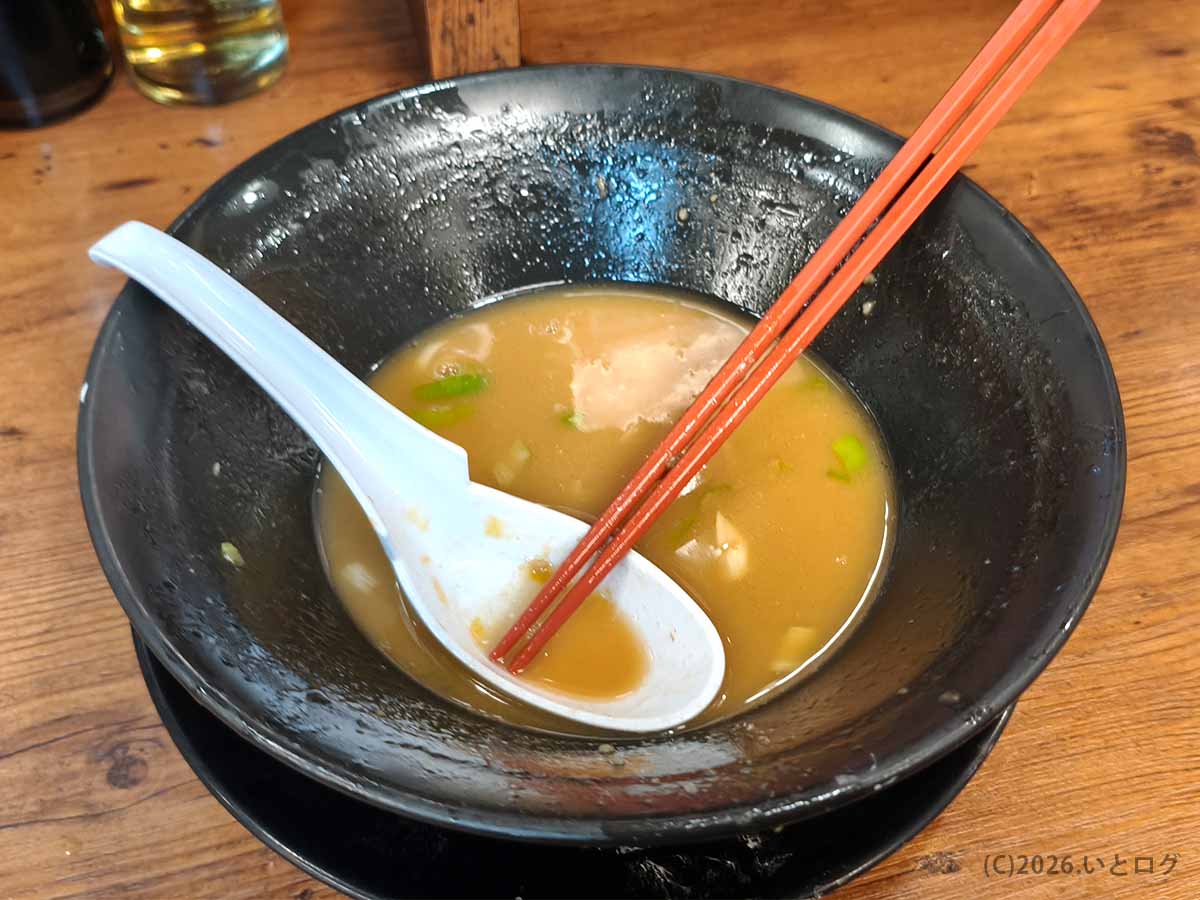 巣鴨家の家系ラーメンを食べ終えた後の黒い丼。残った豚骨スープにレンゲと箸が置かれている