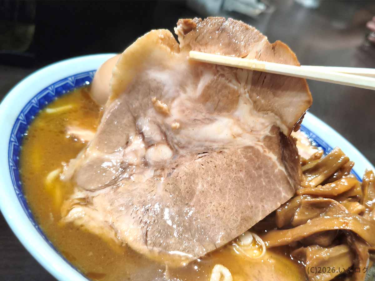 中華そば べんてんのラーメンに入った大きなチャーシューを箸で持ち上げた写真。脂身と赤身が重なる肉厚な一枚