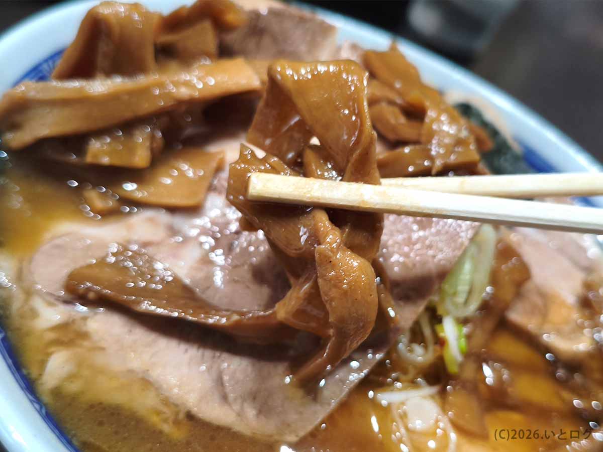 べんてん成増のラーメンにトッピングされたメンマ。濃い茶色に味付けされた幅広のメンマを箸で持ち上げた様子
