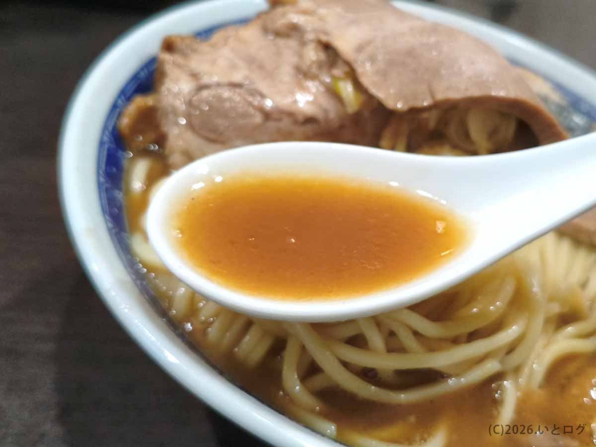 中華そば べんてんのラーメンスープを白いレンゲですくった写真。茶褐色のスープと表面に浮かぶ油分がわかる