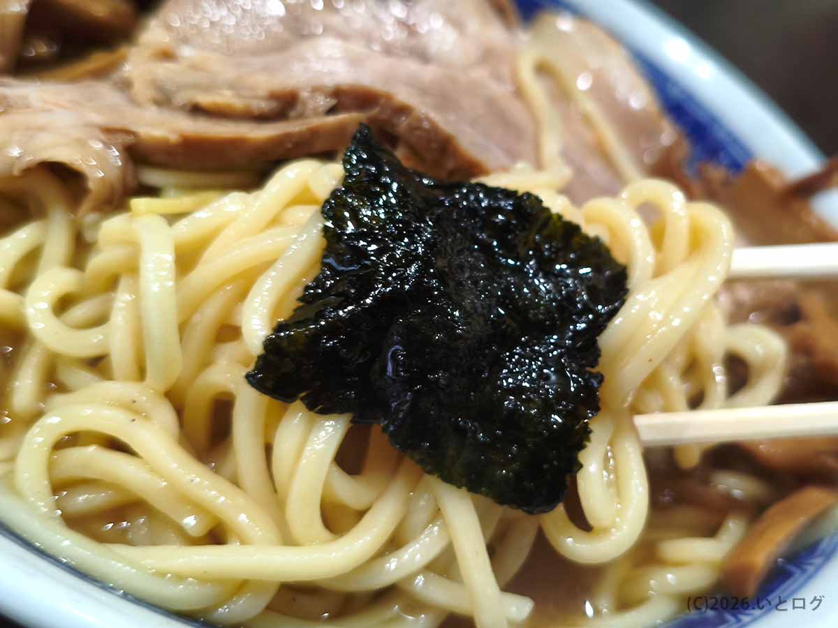 べんてん成増のラーメンで海苔を中太麺に重ねた写真。スープを吸って光沢のある黒い海苔と麺の組み合わせ