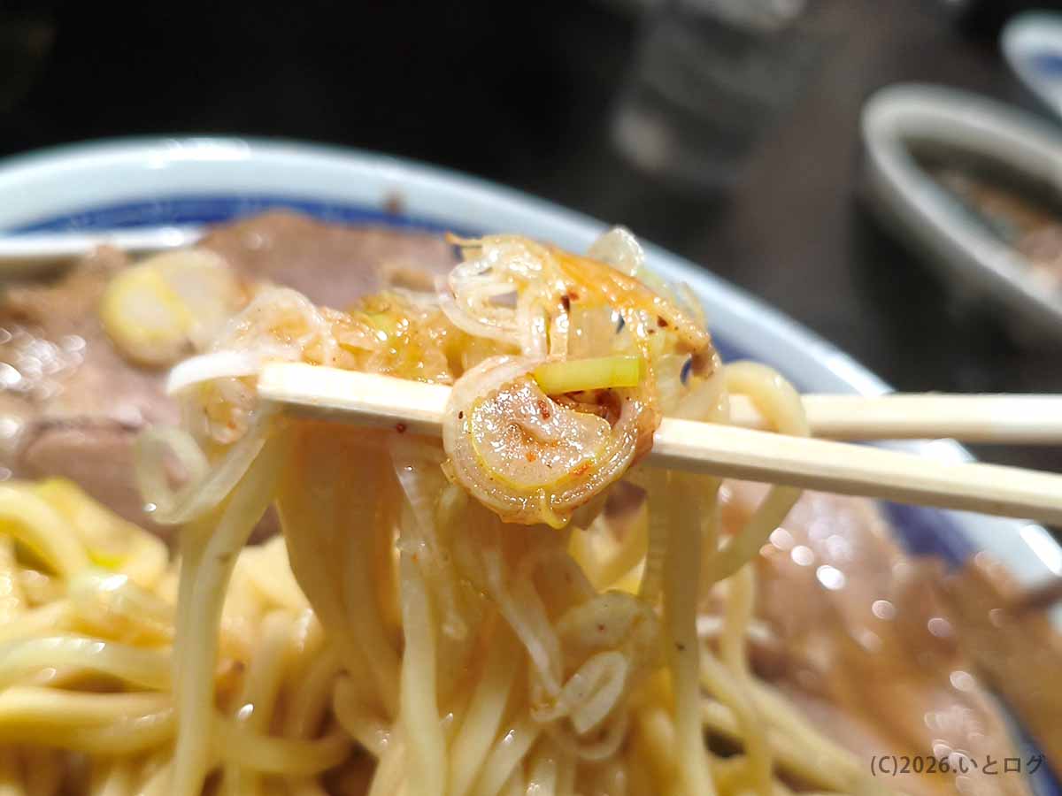 中華そば べんてんのラーメンに盛られた輪切りのネギ。唐辛子がかかったネギを中太麺と一緒に箸で持ち上げた様子