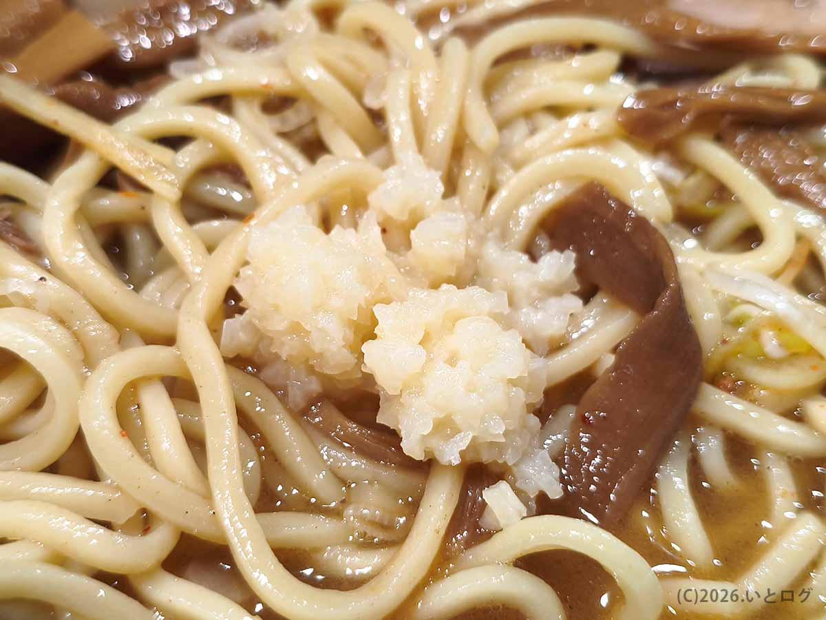 べんてん成増のラーメンに卓上のおろしニンニクを加えた写真。中太麺とメンマの上に白いニンニクが盛られた様子