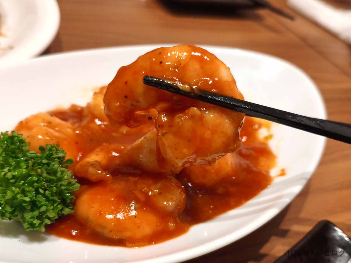甲府市の町中華ダイニング蒔季彩で提供されるエビチリ。赤いチリソースをまとった海老を箸で持ち上げた様子