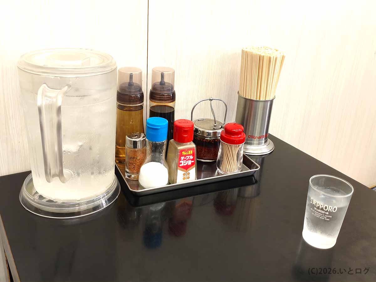 甲府市の中華 福吉のテーブルに置かれたコショウやラー油などの卓上調味料、割り箸、冷水ポットとコップ