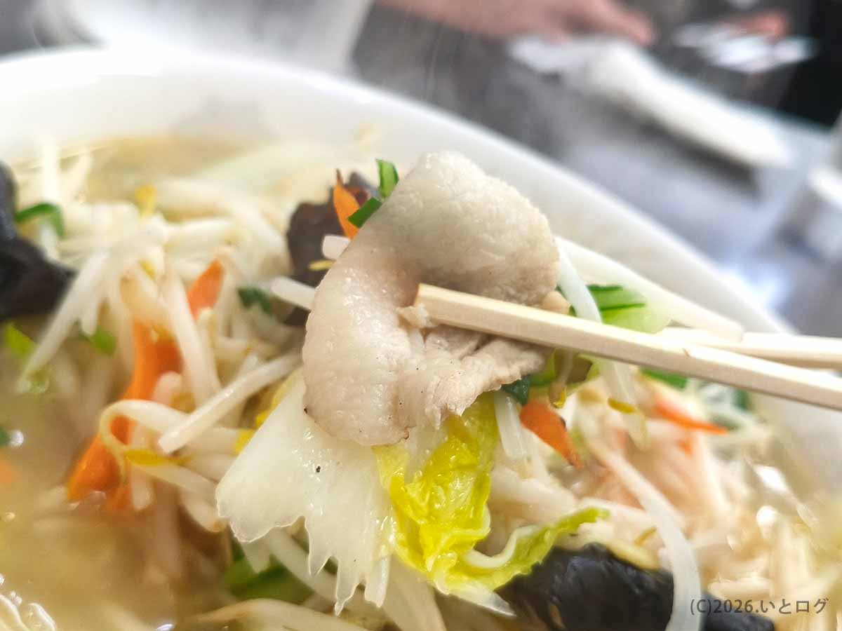 甲府市の中華 福吉のタンメンに入った豚肉と白菜を箸で持ち上げた様子。背景にはもやしやキクラゲなどの野菜が見える