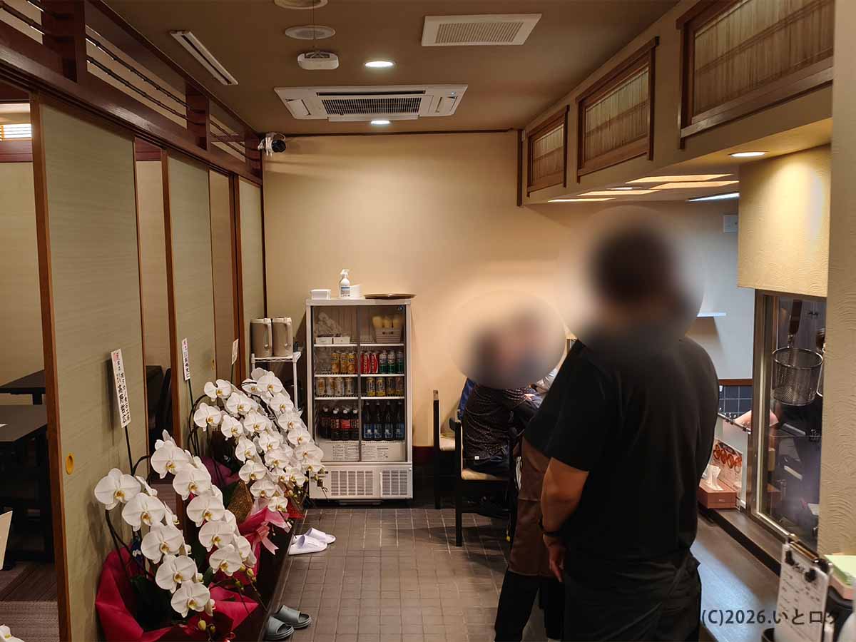 山梨県甲府市朝気のあぶらギルドの店内。木目調の和風内装に開店祝いの胡蝶蘭が並び、奥には飲料冷蔵庫と客席スペースが設けられている。