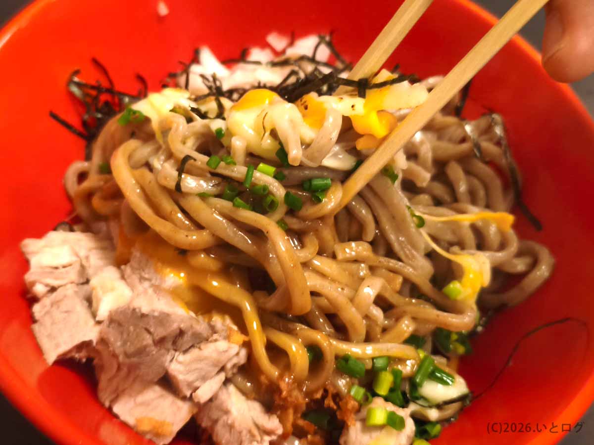 あぶらギルドのBトッピング油そばを箸で混ぜる様子。太麺に卵黄と炙りチーズが絡み、刻み海苔やネギ、チャーシューも見える。
