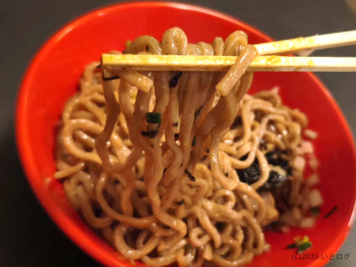 甲府市あぶらギルドの油そばを箸で持ち上げた写真。濃い色のタレが絡んだ太麺にはツヤがあり、刻み海苔やネギも混ざっている。