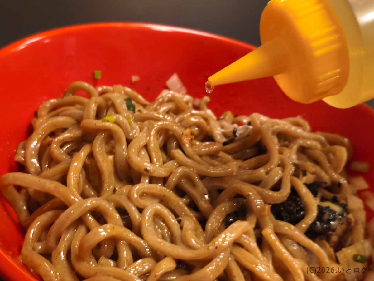 あぶらギルドのBトッピング油そばに卓上の酢を加える様子。チーズと卵黄を混ぜた太麺に酢を垂らし、味の変化を楽しむ。
