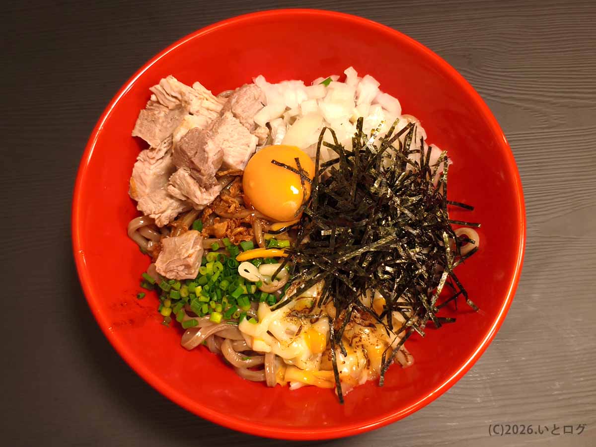 甲府市朝気のあぶらギルドで提供されるBトッピング油そば。チャーシュー、玉ねぎ、ネギ、刻み海苔、卵黄、チーズが彩りよく盛り付けられている。