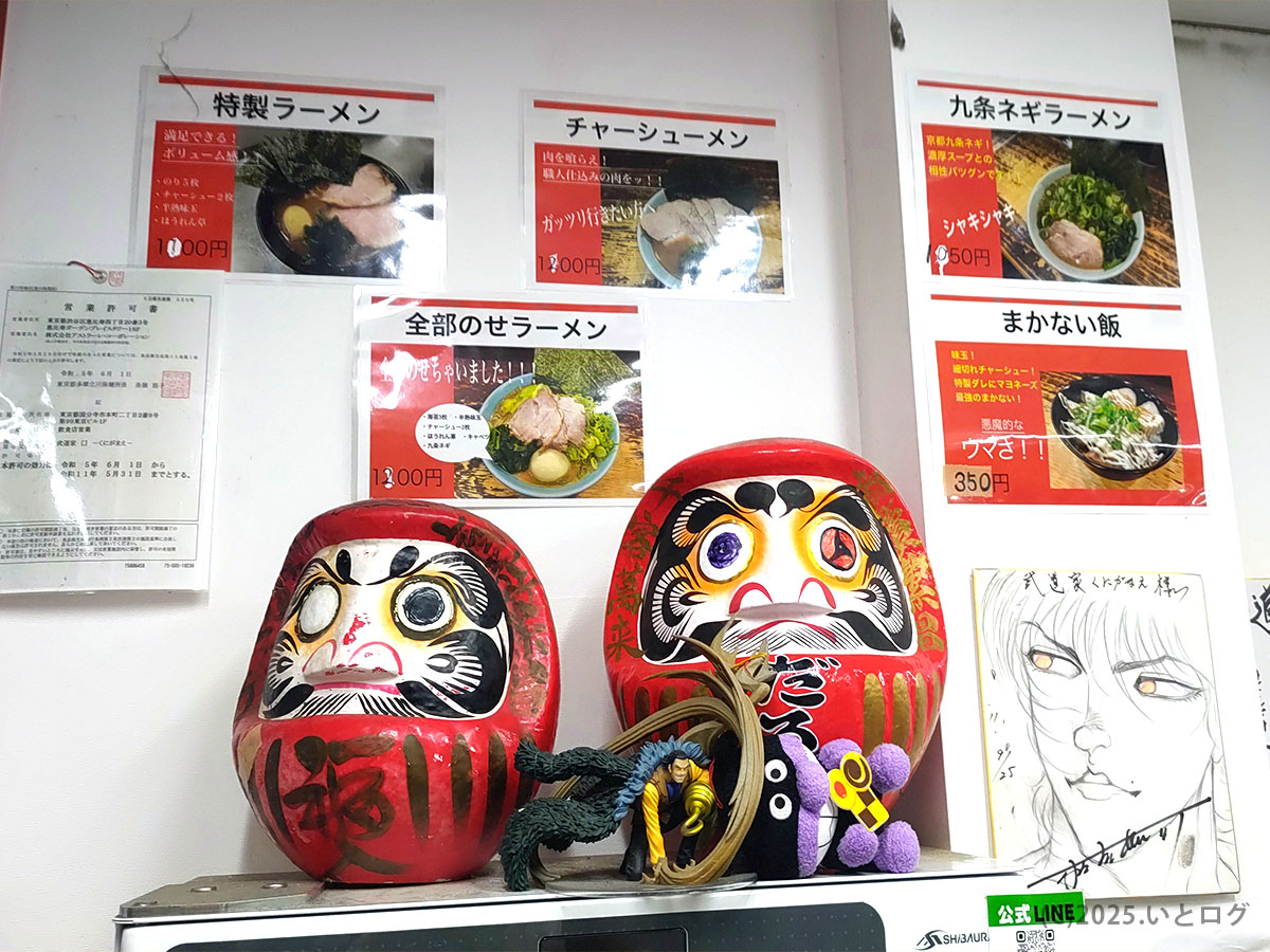 武道家 口(くにがまえ)国分寺の店内掲示。特製ラーメンや九条ネギラーメンなどのメニュー写真と、武道家系統の絆を感じる達磨が飾られた印象的なインテリア。
