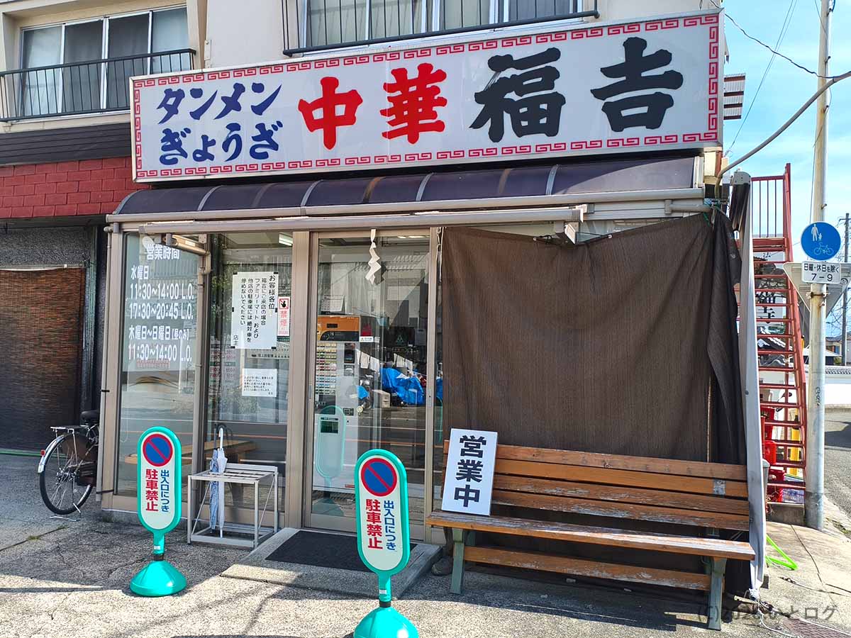 山梨県甲府市上石田にある中華 福吉の外観。タンメン・ぎょうざと書かれた大きな看板と入口前の待合ベンチ