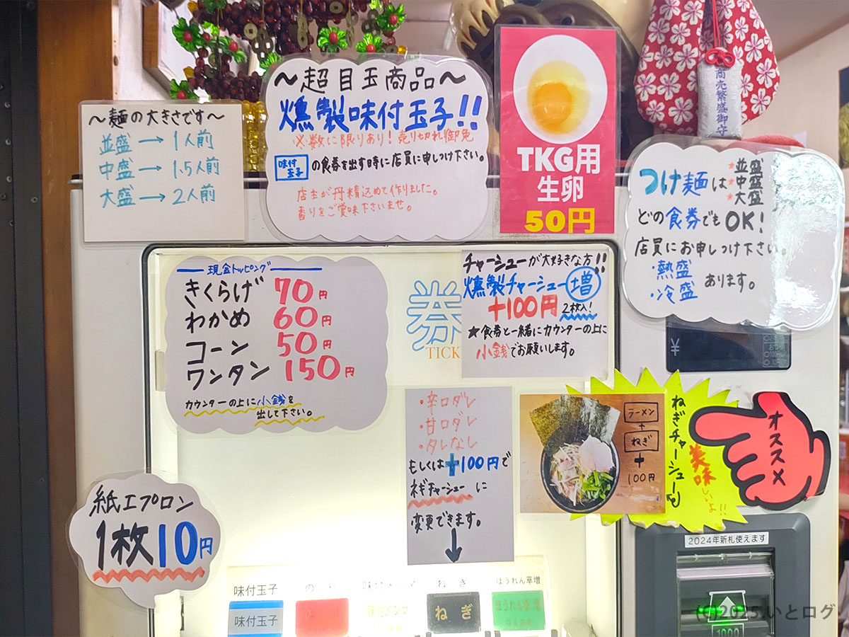 はじめ家の店内掲示。麺の量やつけ麺対応、燻製味付玉子や焼豚増量など人気トッピングの案内が手書きで貼られている。