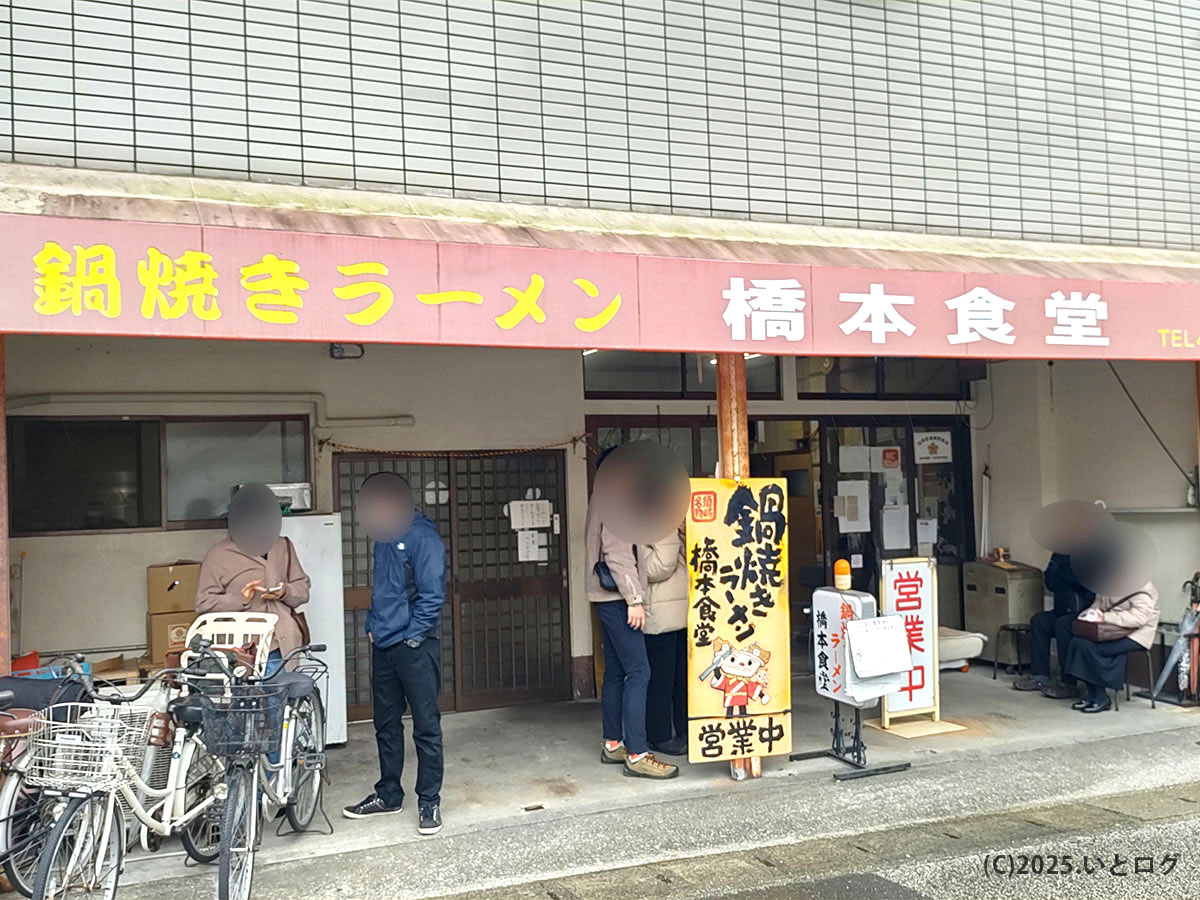 『鍋焼きラーメン 橋本食堂』と書かれた赤いテントの本店外観。開店前から須崎の常連と観光客が行列し、駐車場も満車寸前。