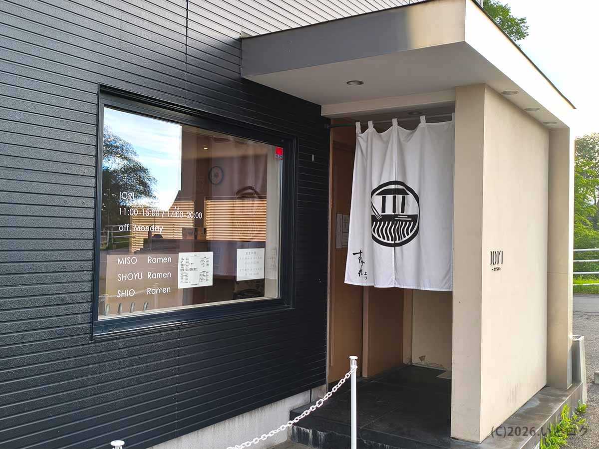 北海道千歳市住吉にあるラーメン店IOrI(イオリ)の外観。黒い外壁と白い暖簾が特徴で、入口横の窓には営業時間やラーメンの種類が掲示されている。