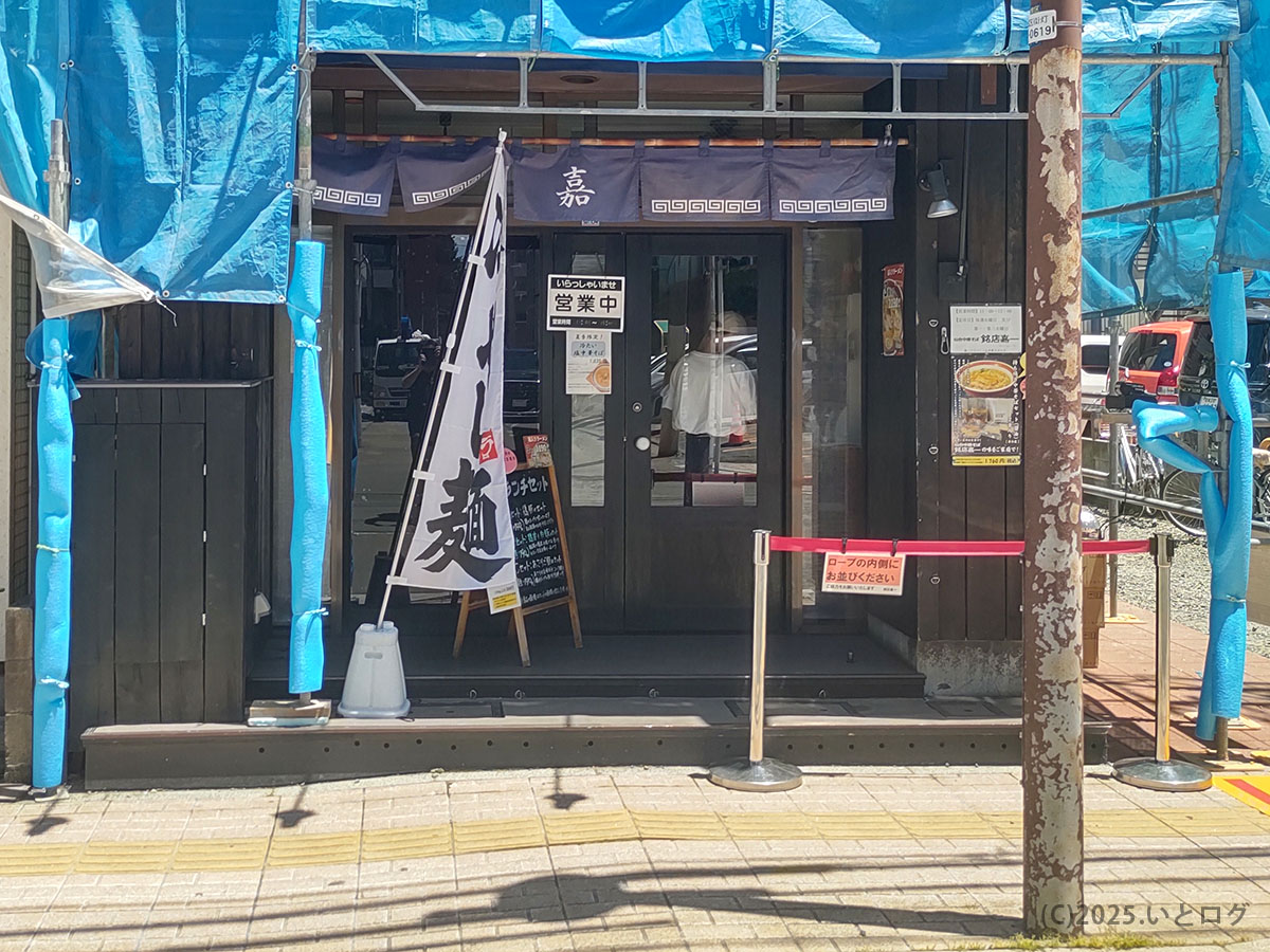 「中華そば 嘉一 国分町店」の外観。のれんには「嘉一」の文字が入り、仙台市国分町で本店の味を受け継ぐ注目店。青い養生シートに囲まれた中でも、暖簾が存在感を放つ。