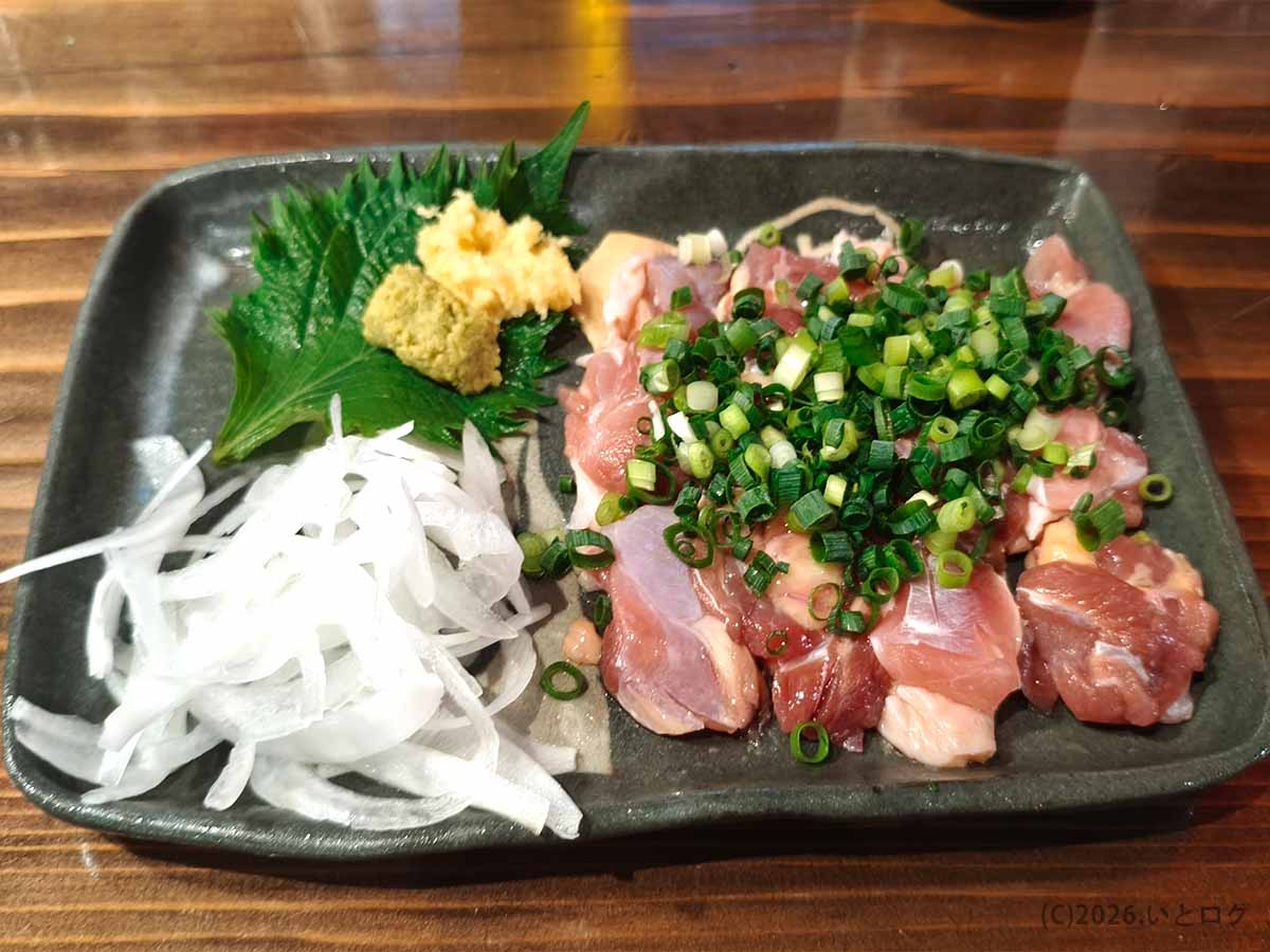 丸万焼鳥 支店の鳥刺し。鶏肉に刻みねぎをのせ、スライスした玉ねぎ、生姜、大葉が添えられている