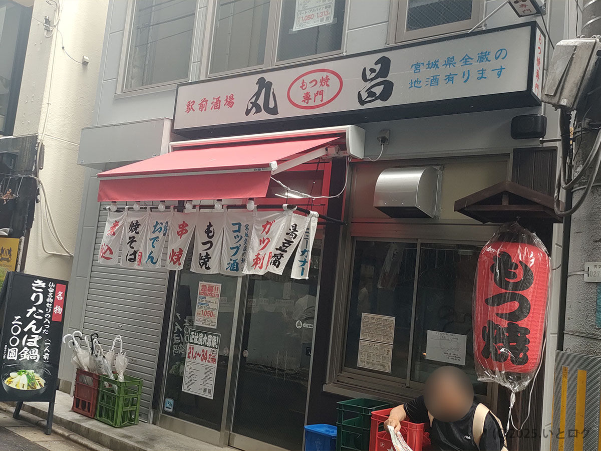 仙台駅近くの路地にある『もつ焼き 丸昌』の外観。赤いテントとのれん、提灯が目印で、仕事帰りにふらりと立ち寄りたくなる雰囲気のもつ焼き専門店
