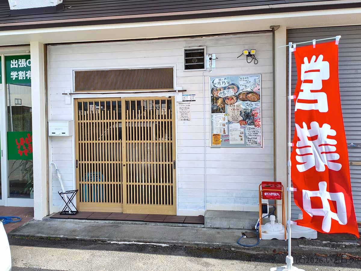 山梨県南アルプス市にある「麺と酒 月乃家」の店舗正面外観。白い木目調の壁に和風の引き戸があり、「営業中」の赤い幟（のぼり）が立っている様子。