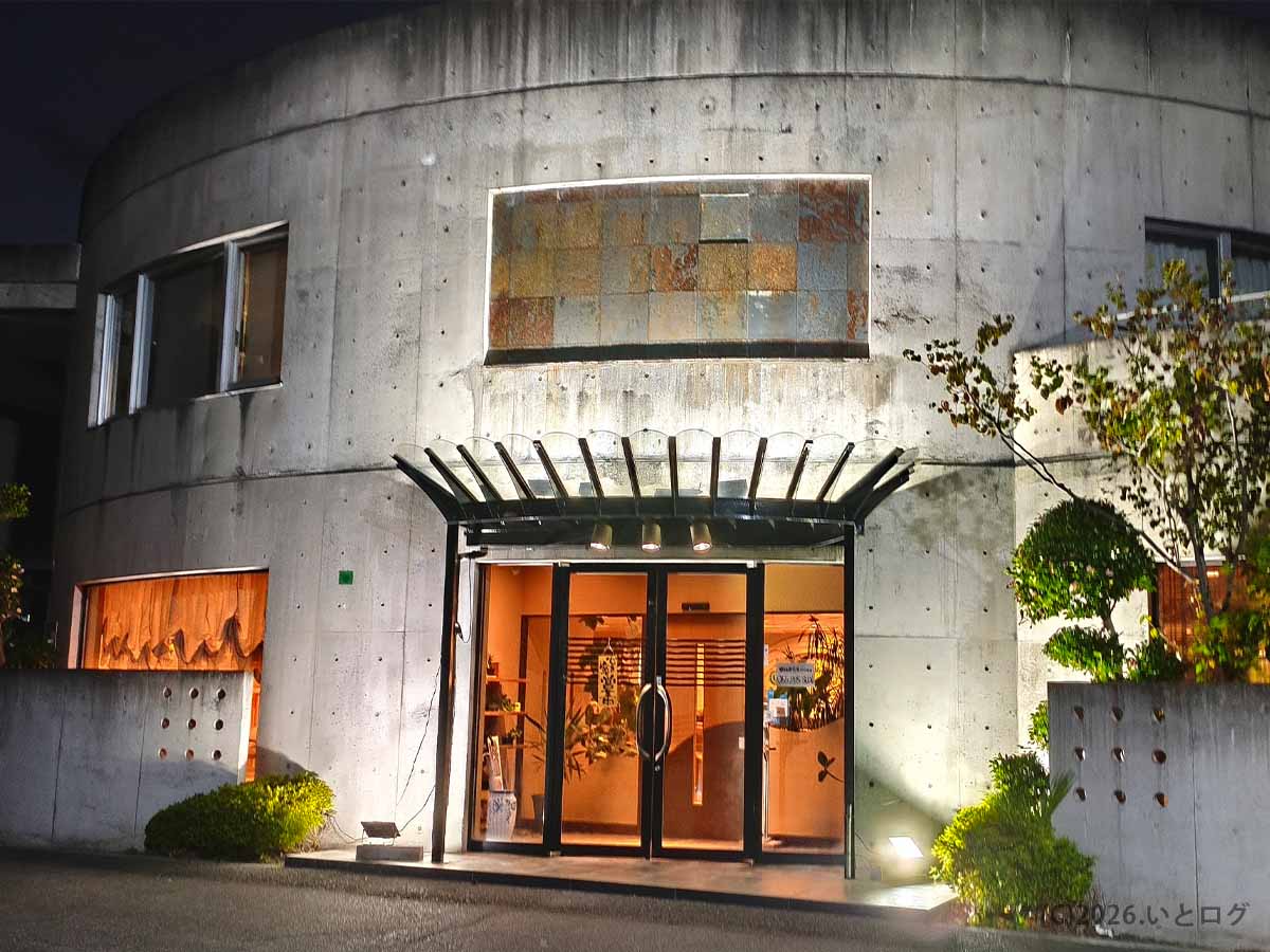 山梨県昭和町にある二代目たわらの夜の外観。曲線を描くコンクリートの建物にガラス張りの入口があり、店内の明かりが見える