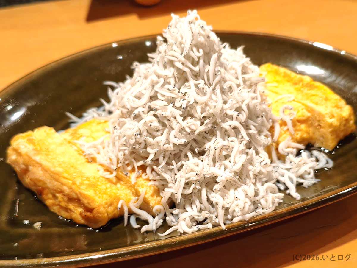二代目たわらのしらすのだし巻き卵。黒い長皿に二切れの厚焼き卵が並び、その中央に大量のしらすが山のように盛られている