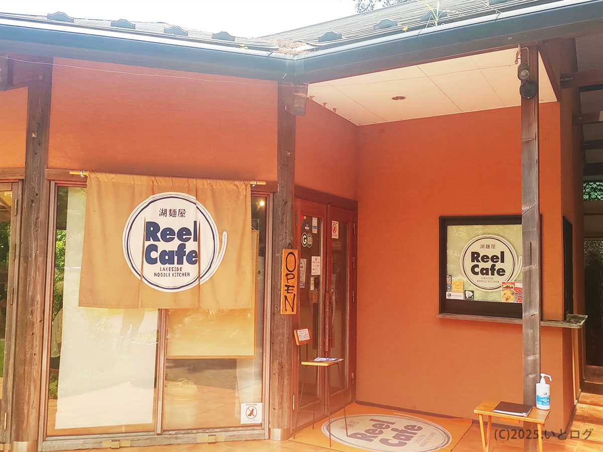暖簾にReel Cafeロゴが映える山中湖畔の外観。入口前は駐車場からすぐ、ドライブ客にも優しいアクセス。