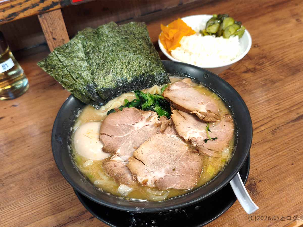 巣鴨家で注文した家系ラーメンと無料ライス。チャーシュー、味玉、ほうれん草、海苔が盛られ、奥には漬物を添えたご飯が並ぶ