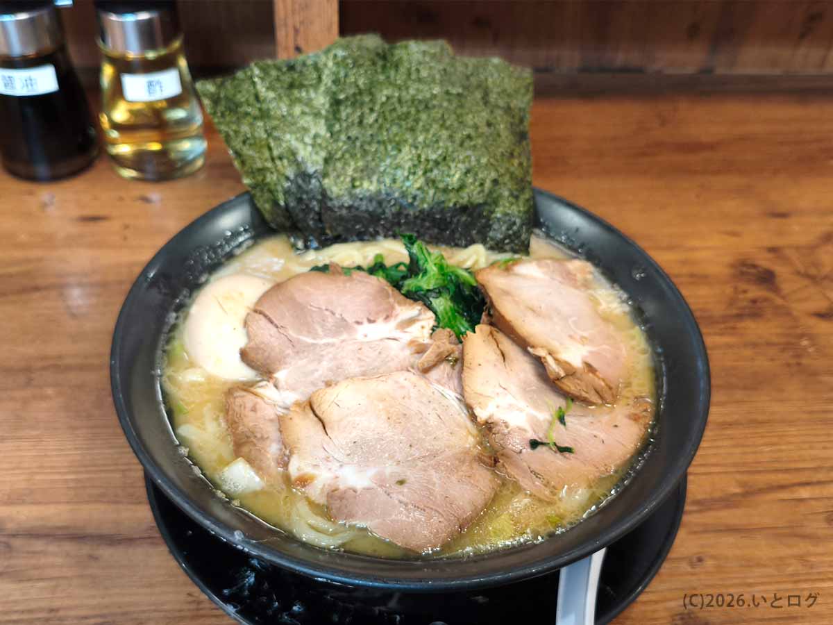 横浜家系ラーメン巣鴨家の豚骨ラーメン。黒い丼に大きなチャーシュー、味玉、ほうれん草、海苔が盛り付けられている