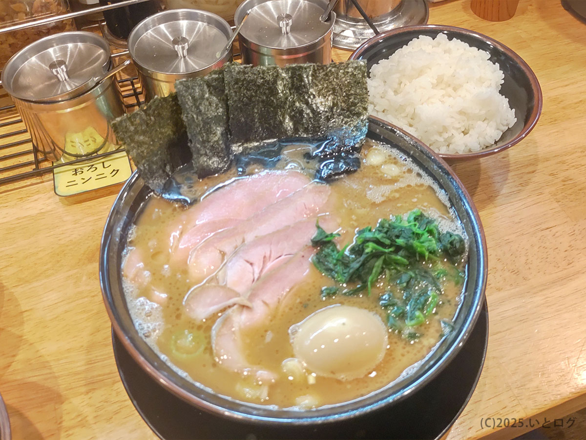 王道鈴家の家系ラーメン。豚骨醤油スープにピンク色のチャーシュー、ほうれん草、海苔が並び、濃厚な香りが立ち上る。伊豆の国市で人気の王道家直系ラーメンを白飯と一緒に楽しむ一杯。