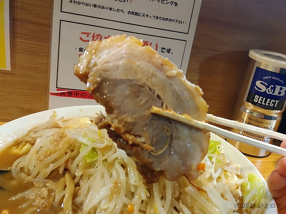 箸で持ち上げた厚切りチャーシューのとろける断面。コール次第でトッピング量も変わる鷹の目スタイルを象徴する一枚。