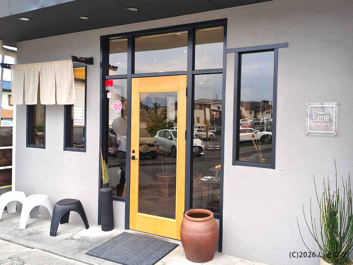 黄色い木製ドアとのれんが目印になった、山梨県甲府市のラーメン店「上田屋」の入口