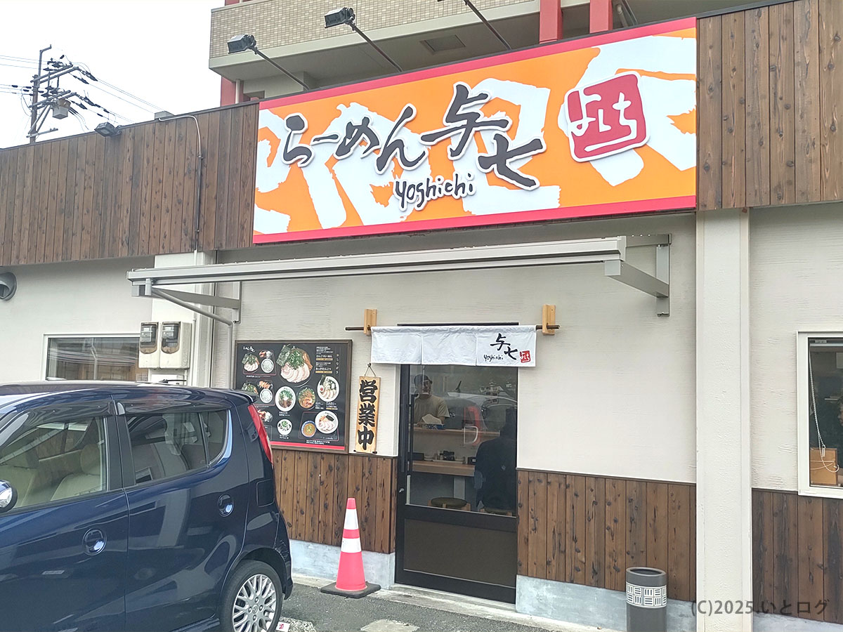 滋賀県大津市にあるらーめん与七 堅田店の外観。オレンジ色の大きな看板が目を引き、暖簾のかかった入口の前には駐車場スペースが用意され、車での来店もしやすい。